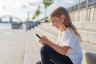 Şehirde sokakta oturan kız çocuğu cep telefonu kullanıyor.. 