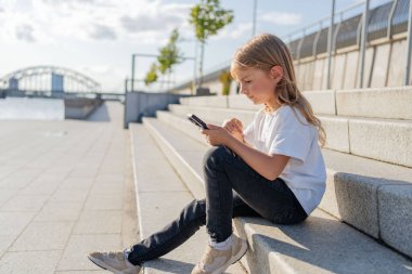 Şehirde sokakta oturan kız çocuğu cep telefonu kullanıyor.. 