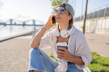 Genç İspanyol hippi kız elinde içecekle sokakta otururken cep telefonunu karıştırıyor.. 