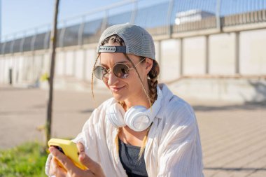 Genç İspanyol hippi kız elinde içecekle sokakta otururken cep telefonunu karıştırıyor.. 