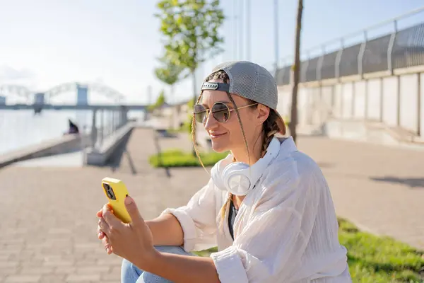 若いヒスパニックヒップスター少女はテイクアウト飲料で通りに座っている間携帯電話をブラウズ — ストック写真