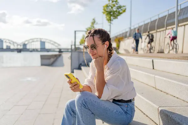 笑顔の美しい女性が携帯電話を持ち 音楽を聴き ストリートでビデオを見ている 外でショッピングモバイルアプリを使用してハッピーヒップスター女性 — ストック写真