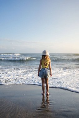 Çocuk Bali 'deki tropikal deniz sahillerinde eğleniyor. Sörf kenarındaki su birikintisinin yanında koşan komik kız. Aktif çocuk yaşam tarzı. 