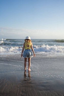 Çocuk Bali 'deki tropikal deniz sahillerinde eğleniyor. Sörf kenarındaki su birikintisinin yanında koşan komik kız. Aktif çocuk yaşam tarzı. 