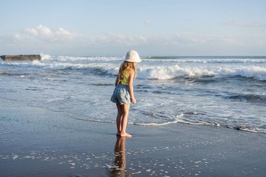 Çocuk Bali 'deki tropikal deniz sahillerinde eğleniyor. Sörf kenarındaki su birikintisinin yanında koşan komik kız. Aktif çocuk yaşam tarzı. 