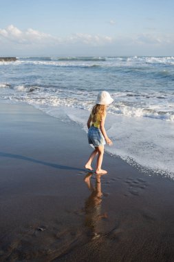Çocuk Bali 'deki tropikal deniz sahillerinde eğleniyor. Sörf kenarındaki su birikintisinin yanında koşan komik kız. Aktif çocuk yaşam tarzı. 