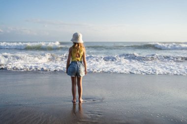 Çocuk Bali 'deki tropikal deniz sahillerinde eğleniyor. Sörf kenarındaki su birikintisinin yanında koşan komik kız. Aktif çocuk yaşam tarzı. 