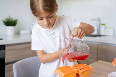 Dondurma yapma süreci. Mutfaktaki tezgahın üstündeki kalıplarda leziz buz lolipopları yapan bir çocuk..