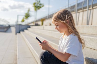 Şehirde sokakta oturan kız çocuğu cep telefonu kullanıyor.. 