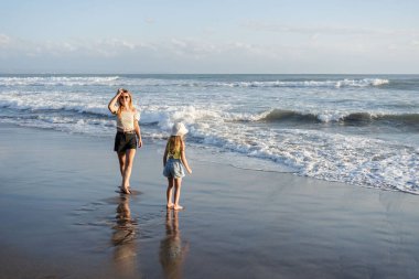 Anne ve kızı Bali 'de kumsalda eğleniyorlar, dalgalarda koşuyorlar, hayatın tadını çıkarıyorlar ve seyahat ediyorlar.