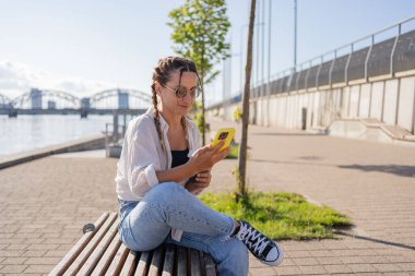Şehir caddesinde oturan hippi bir kadın, selofan kullanıyor, arkadaşlarıyla sohbet ediyor, video görüşmesi yapıyor.