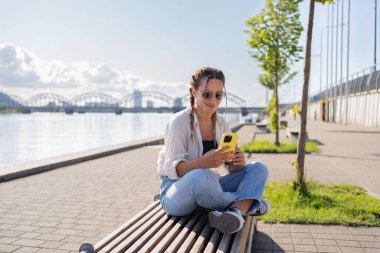 Şehir caddesinde oturan hippi bir kadın, selofan kullanıyor, arkadaşlarıyla sohbet ediyor, video görüşmesi yapıyor.
