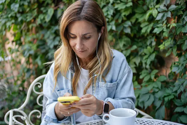 stock image Portrait of cheerful girl typing in mobile while situating at table while listening music in headset. .Lifestyle concept