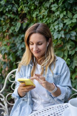  Kulaklık takan ve açık kafede oturup müzik dinleyen bir kadın. Restoranda uzaktan kumandalı çalışan serbest çalışan biri.. 