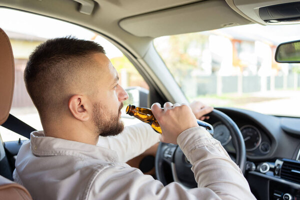 Мужчина пьет алкоголь за рулём машины. Не пить и не водить машину