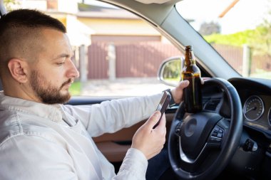 Araba kullanırken elinde cep telefonu ve bira şişesi tutan bir adam. Alkol problemi. Tehlikeli bir sorun. Kaza olasılığı var.