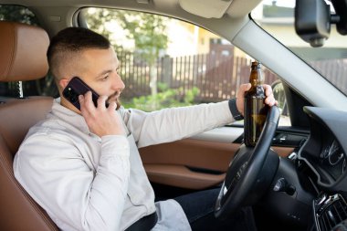 Araba kullanırken elinde cep telefonu ve bira şişesi tutan bir adam. Alkol problemi. Tehlikeli bir sorun. Kaza olasılığı var.