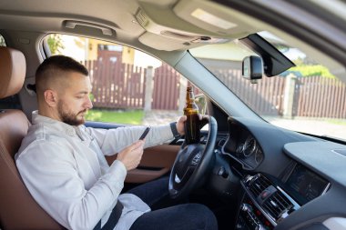 Araba kullanırken elinde cep telefonu ve bira şişesi tutan bir adam. Alkol problemi. Tehlikeli bir sorun. Kaza olasılığı var.