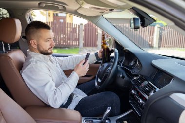Araba kullanırken elinde cep telefonu ve bira şişesi tutan bir adam. Alkol problemi. Tehlikeli bir sorun. Kaza olasılığı var.