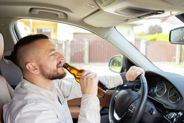 Мужчина пьет алкоголь за рулём машины. Не пить и не водить машину