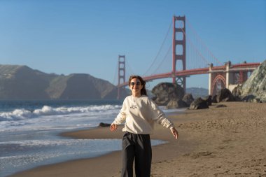Sahilde yürüyen genç bir kadın Golden Gate, San Francisco 'ya bakıyor. . 