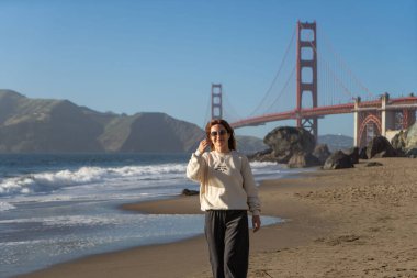 Sahilde yürüyen genç bir kadın Golden Gate, San Francisco 'ya bakıyor. . 