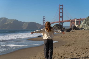 Sahilde yürüyen genç bir kadın Golden Gate, San Francisco 'ya bakıyor. . 