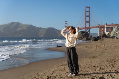 Sahilde yürüyen genç bir kadın Golden Gate, San Francisco 'ya bakıyor. . 