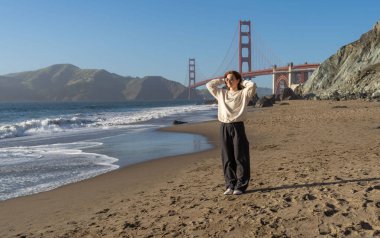 Sahilde yürüyen genç bir kadın Golden Gate, San Francisco 'ya bakıyor. . 