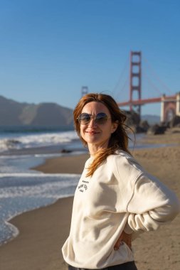 Sahilde yürüyen genç bir kadın Golden Gate, San Francisco 'ya bakıyor. . 