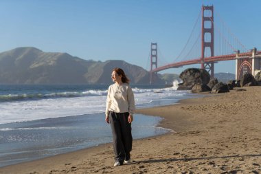 Sahilde yürüyen genç bir kadın Golden Gate, San Francisco 'ya bakıyor. . 
