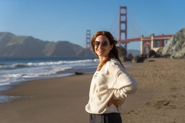 Sahilde yürüyen genç bir kadın Golden Gate, San Francisco 'ya bakıyor. . 
