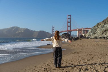 Sahilde yürüyen genç bir kadın Golden Gate, San Francisco 'ya bakıyor. . 