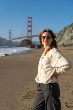 Sahilde yürüyen genç bir kadın Golden Gate, San Francisco 'ya bakıyor. . 