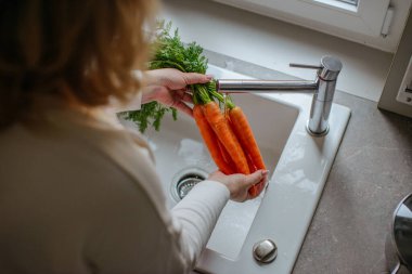 Asyalı genç bir kadın havuç, domates, brokoli taze sebze, biber suyu ve lavaboda su sıçratma havuzu yıkıyor, taze salata hazırlıyor, yemek pişiriyor. Sağlıklı yiyecekler..