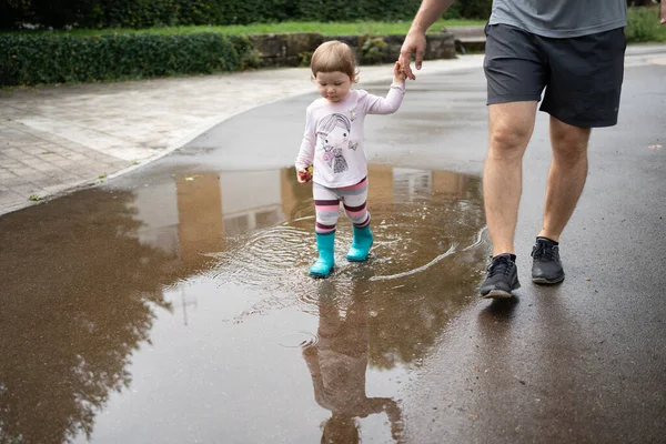 daughter and daddy walking through puddles in the park.