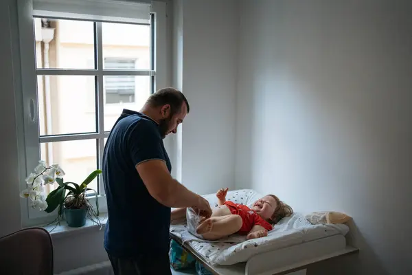 Baba, evde küçük çocuğuna bakıyor masa değiştiriyor, giysi değiştiriyor. Babalar Günü konsepti, gerçek aile kavramı.