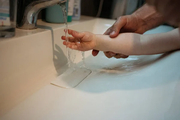 Baba, kızının ellerini küvette yıkamasına yardım ediyor. Çocuklarla ilgilenme kavramı.