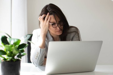 Gözlüklü, çalışanı ya da öğrencisi olan ciddi bir profesyonel iş kadını dizüstü bilgisayar kullanıyor ve çok üzgün.