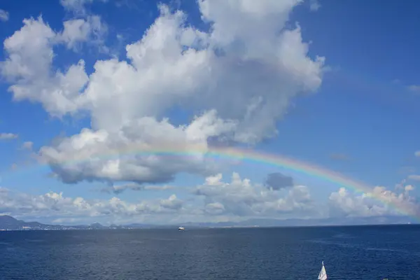 Okyanusun üzerinde gökkuşağı, mavi gökyüzü, bulutlar ve yağmur bulutları