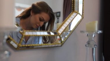 Aynanın önündeki pijamalı kadın makyajını yaptırıyor.