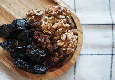 Tahta bir tabakta, kareli masa örtüsünde kurumuş meyve ve fındık.                               