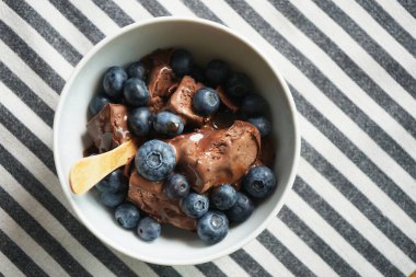 Çikolata soslu dondurma ve çizgili masa örtüsü üzerinde yabanmersini.                               