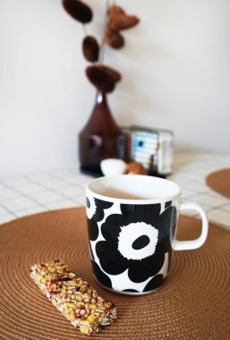 Bir fincan çay ve açık renkli bir yemek masasında mısır gevreği.                                