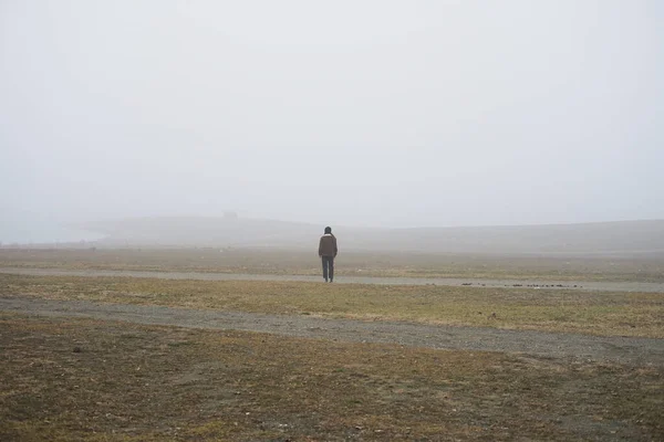 Stock image  A lonely man stands in a field covered with white fog