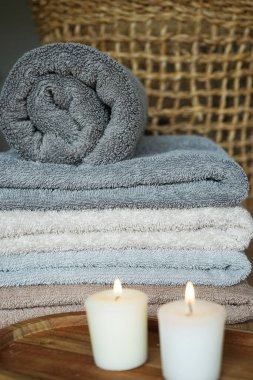 Mumların yanında gri ve bej renkli havlu yığını ve hasır bir sepet.