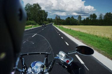 Bir motosikletli asfalt yolda, ormanın ve bulutların arkasında.