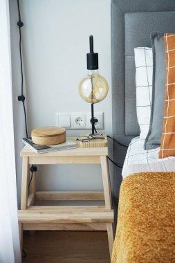 Penceresinde lamba ve dekor olan ahşap bir masa ve kareli keten ve kahverengi ekose kumaşlı bir yatak.