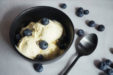 Kaşık yanında siyah tabakta taze yaban mersinli dondurma.