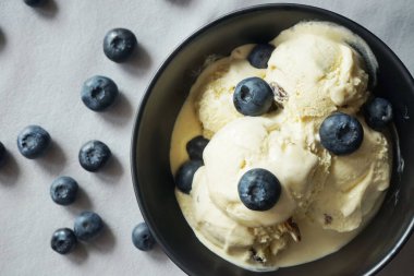 Kaşık yanında siyah tabakta taze yaban mersinli dondurma.